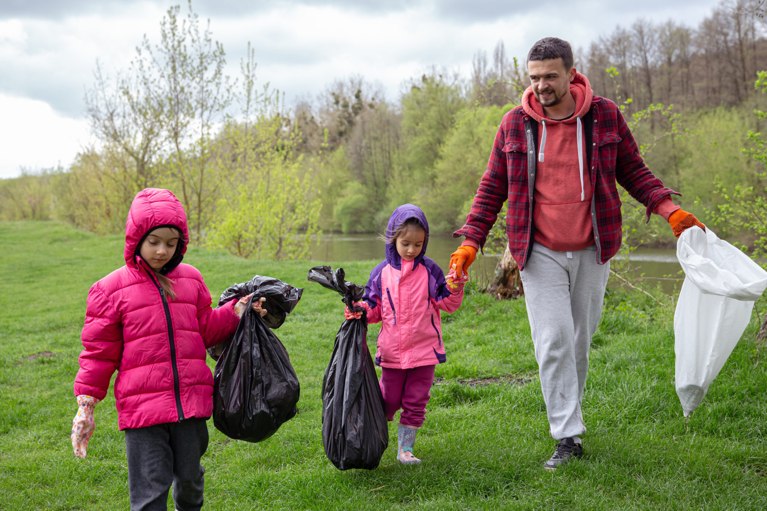 Two little girls with their dad, with garbage bags on a trip to nature, are cleaning the environment.