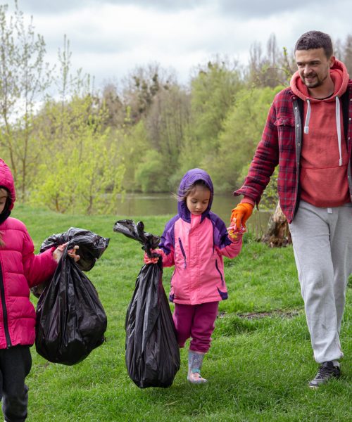 Two little girls with their dad, with garbage bags on a trip to nature, are cleaning the environment.